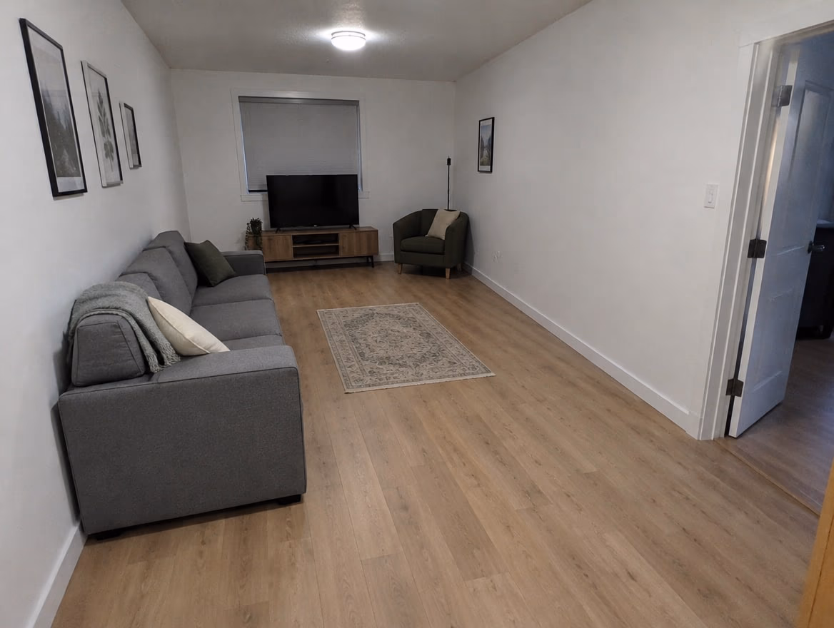 A long narrow living room with the sofa against the wall, a small floating rug and an empty middle
