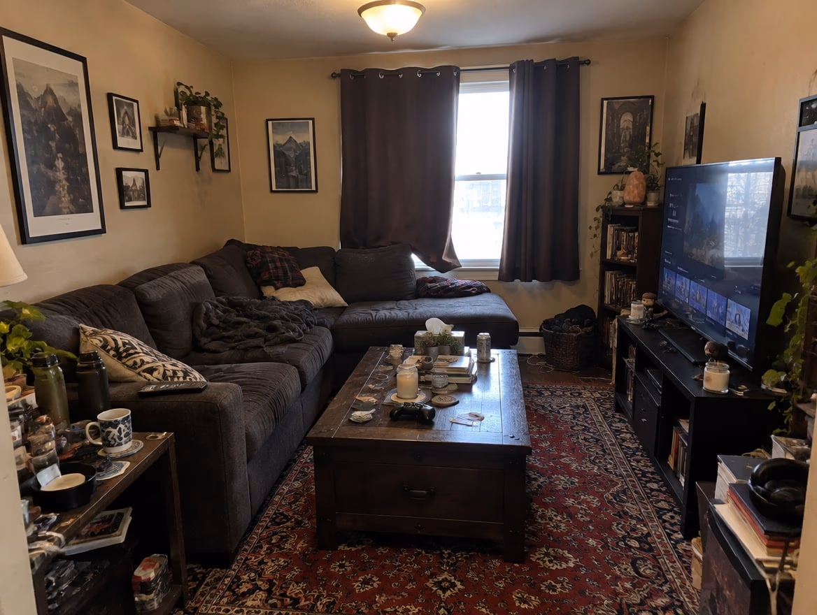 A cramped small living room with a bulky dark sectional, heavy curtains and a busy rug