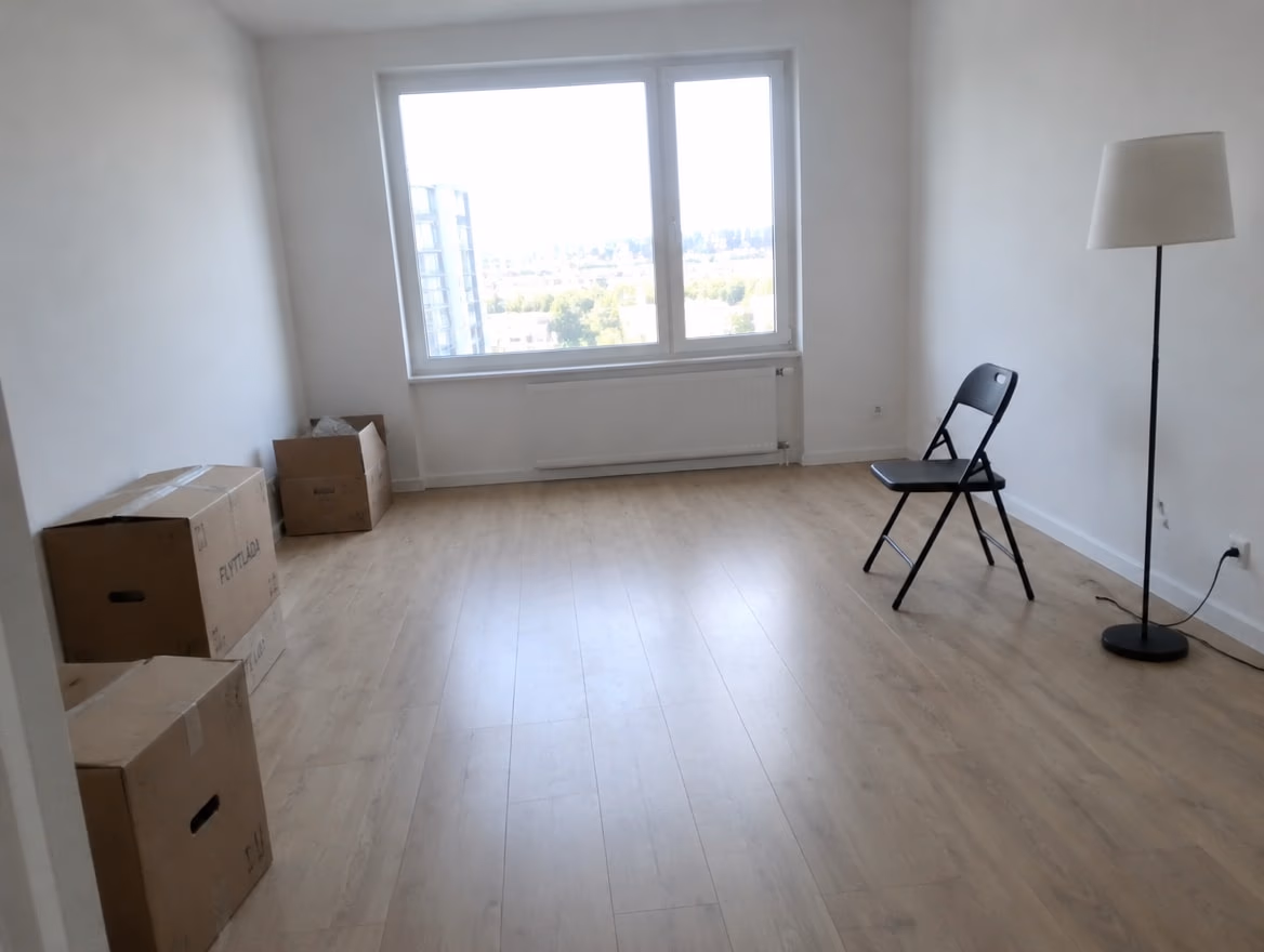 An almost empty new living room with bare walls, moving boxes and a folding chair